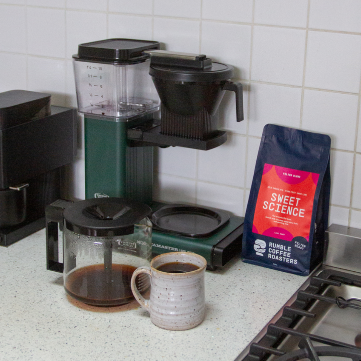 Coffee making setup with moccamaster, mug full of coffee, and a bag of Rumble Coffee Sweet Science filter blend.